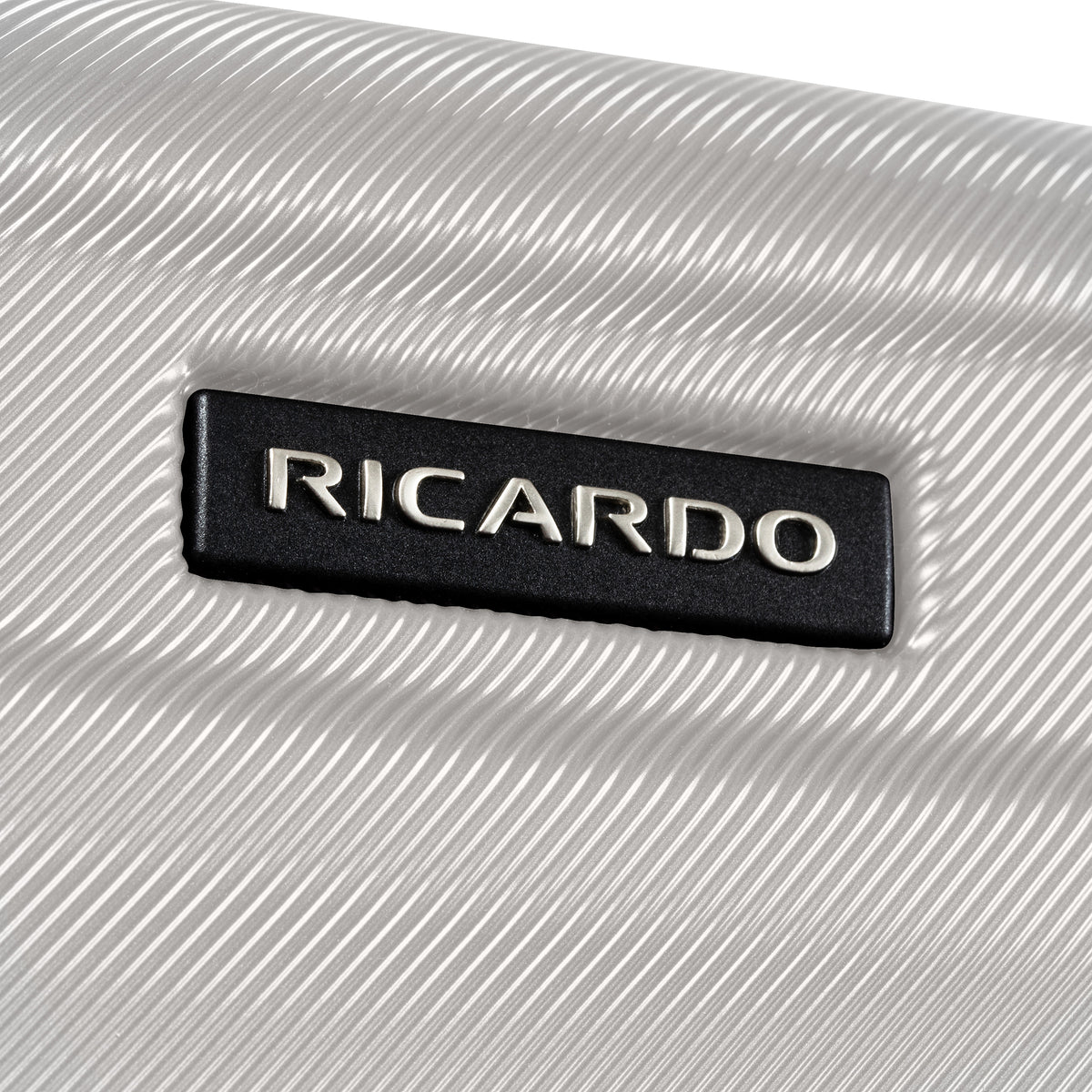Close-up of a textured silver hard case with a black rectangular badge embossed with the brand name RICARDO in silver lettering.