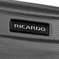 Close-up of a textured black suitcase or hard case with a rectangular black badge featuring the silver metallic brand name RICARDO.